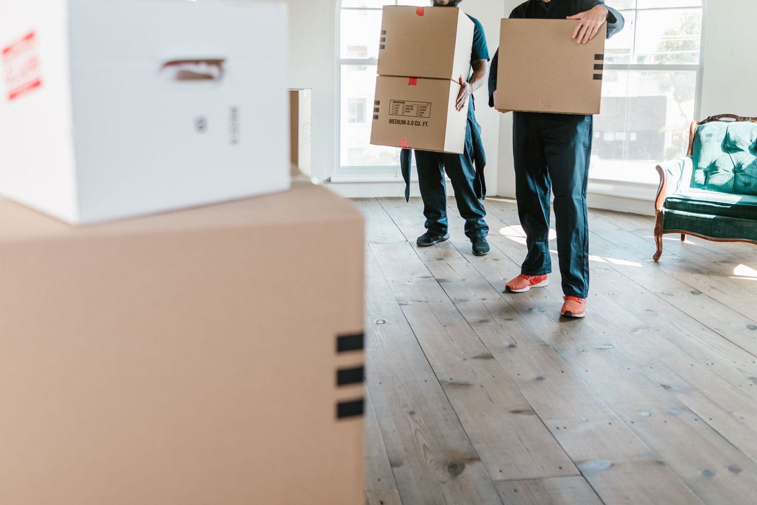 Two movers in uniform carrying boxes in a bright, new home setting.
