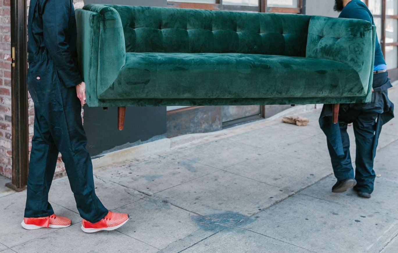 Two men carrying a green sofa on a city street, showcasing teamwork and moving services.