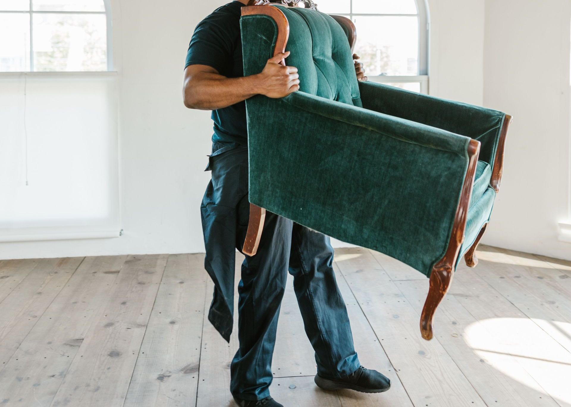African American man carrying armchair in a bright, empty room, symbolizing moving day.